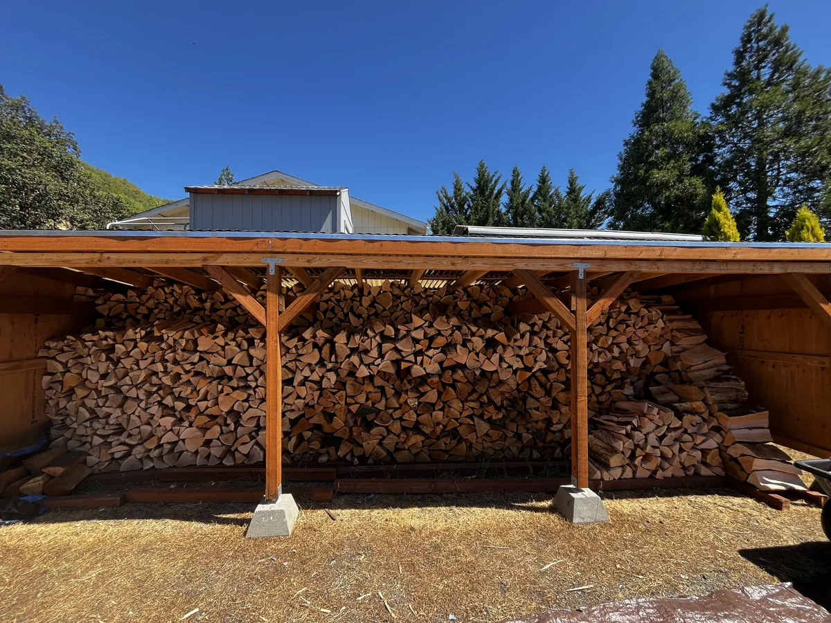 Split firewood stacked wall to wall and squared off under a covered wood shed on a Southern Oregon property
