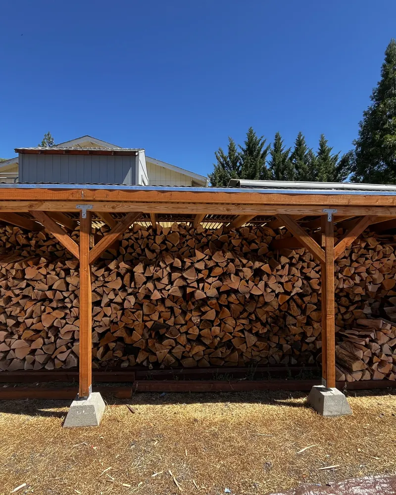 Split firewood stacked wall to wall and squared off under a covered wood shed on a Southern Oregon property