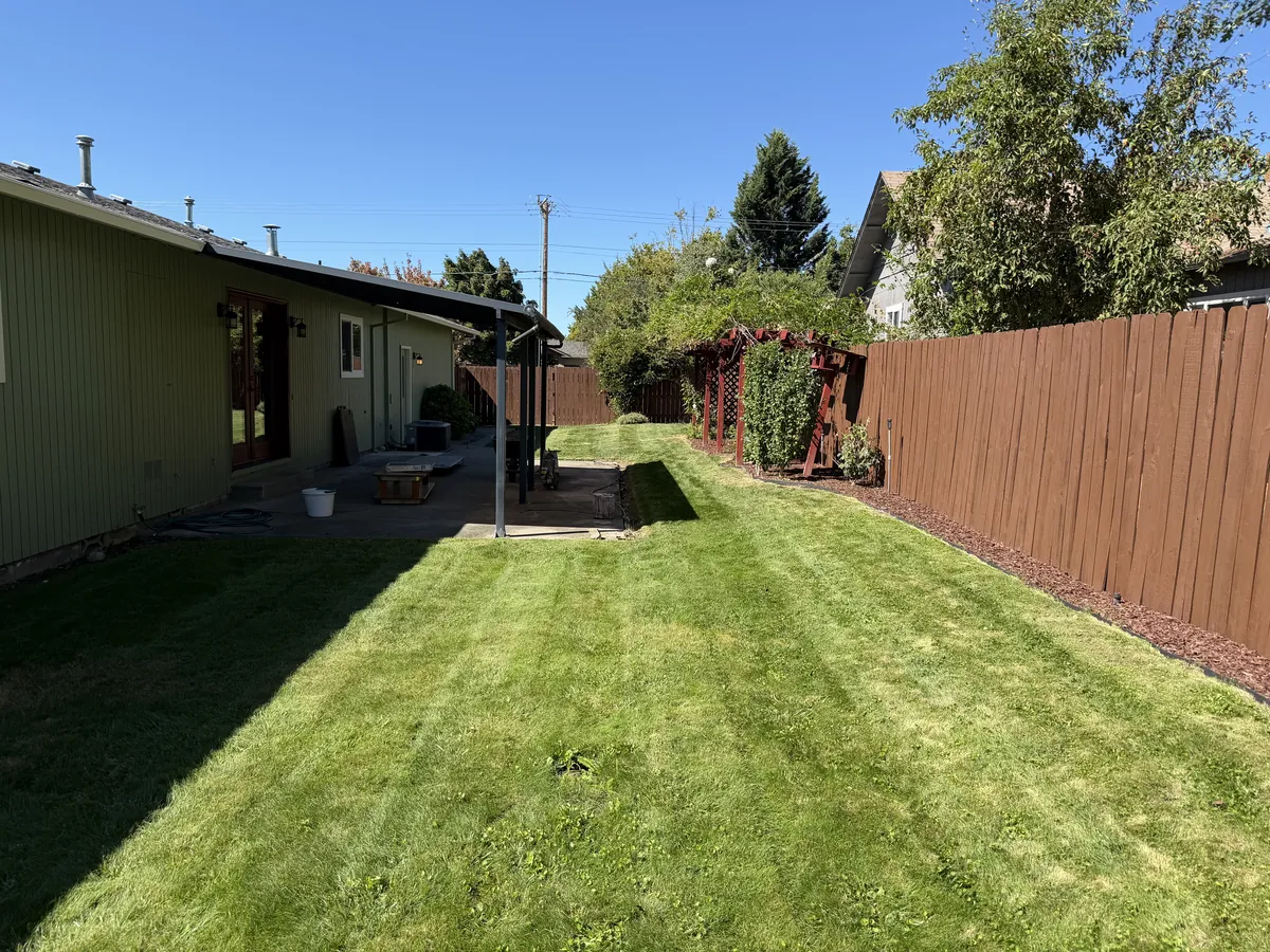 Freshly mowed backyard lawn with clean mower stripes and new red bark spread along the fence line at a Southern Oregon home