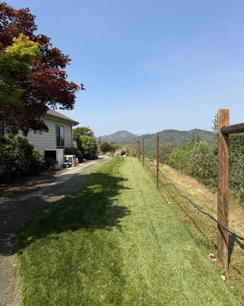 Strip of freshly cut lawn beside a gravel driveway on a hillside property with Southern Oregon ridgelines in the background
