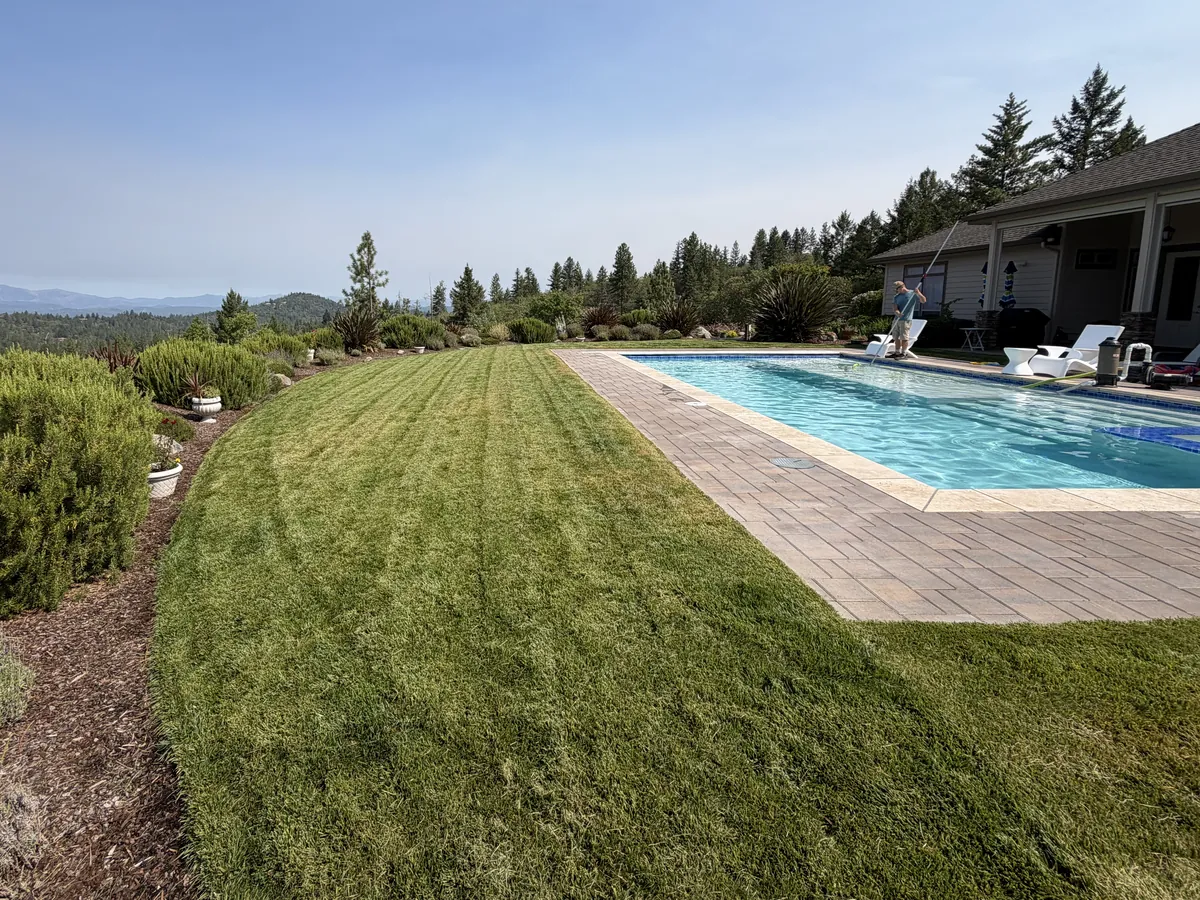 Freshly mowed lawn with clean mower stripes running along a poolside patio on a hilltop property in Southern Oregon
