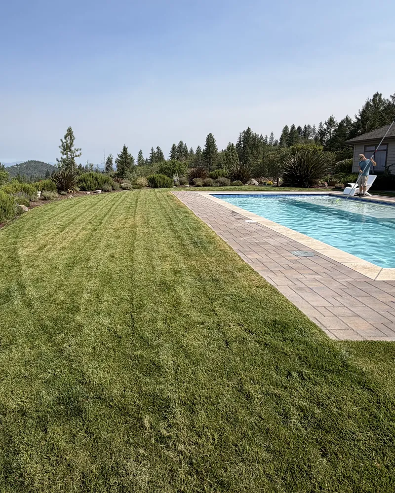 Freshly mowed lawn with clean mower stripes running along a poolside patio on a hilltop property in Southern Oregon