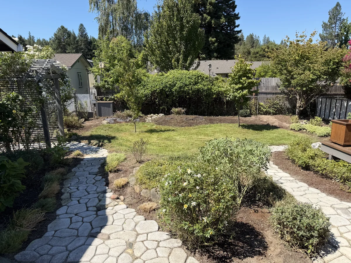 Backyard with fresh dark mulch in the planting beds, paver stone pathways, roses and young trees after a Hilltop cleanup in Southern Oregon