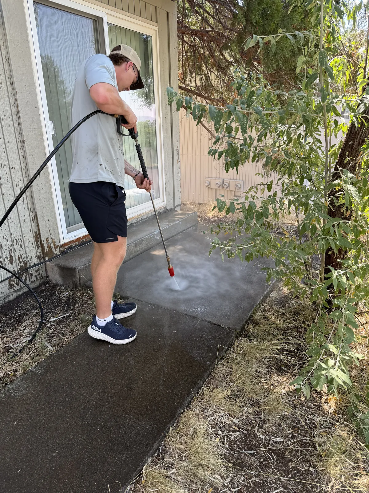 Hilltop Landscaping crew member pressure washing built-up grime off a concrete patio and walkway at a Southern Oregon home