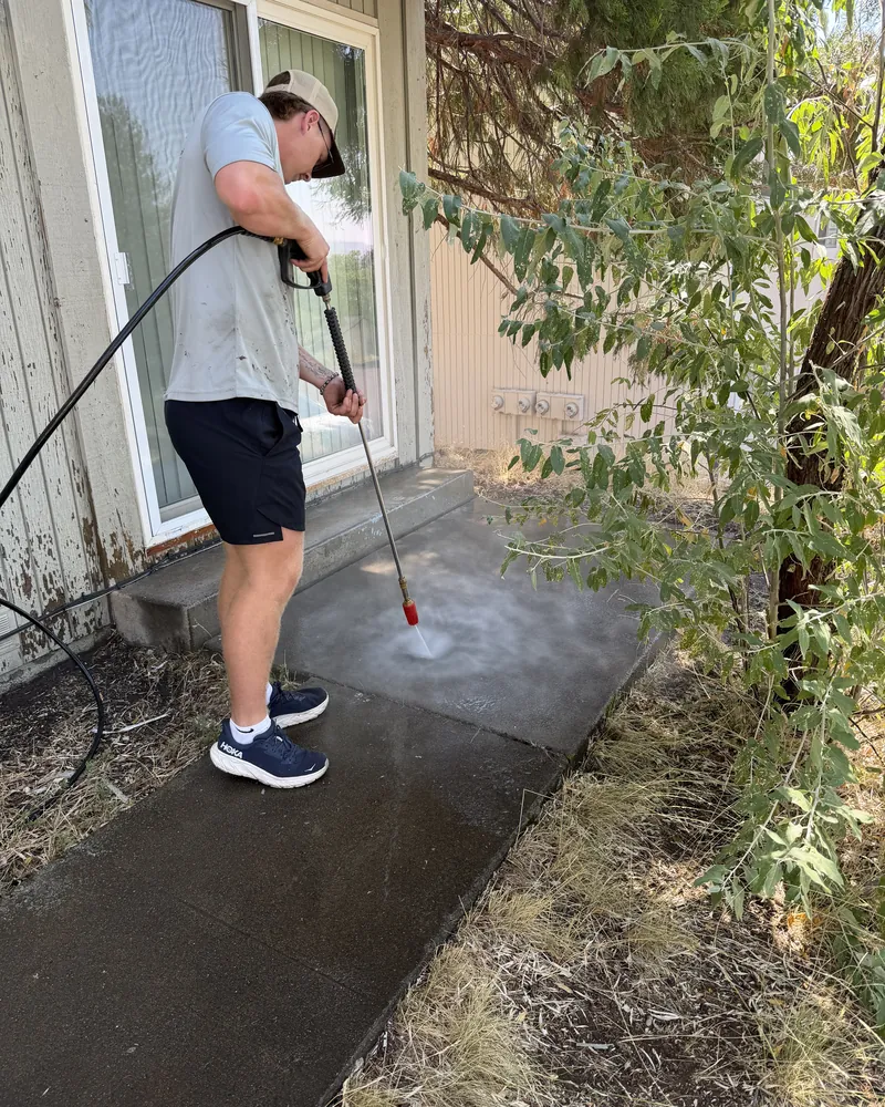 Hilltop Landscaping crew member pressure washing built-up grime off a concrete patio and walkway at a Southern Oregon home